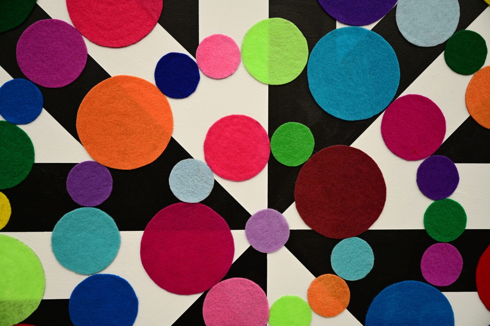 Close-up of a colorful abstract artwork featuring overlapping felt circles in various sizes on a black and white geometric patterned background.
